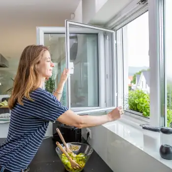 Frau öffnet Fenster mit eingesetztem Drehfenster Spannrahmen in der Küche